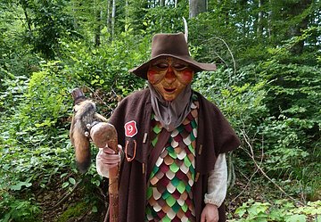 Sagenweg Huaterle Die Wemdinger Sagengestalt "Huaderle" steht mit einem braunen Gewand im Wald.