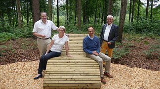Vier Personen sitzen auf einer Liegebank im Wald