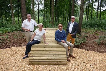 Vier Personen sitzen auf einer Liegebank im Wald
