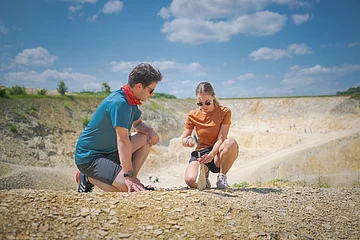 Ein Mann im blauen Shirt kniet neben einer Frau, die mit Hammer und Meißel vorsichtig eine Steinplatte im Fossiliensteinbruch Blumenberg teilt.