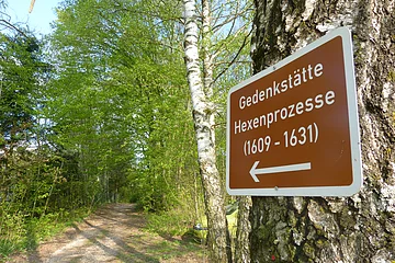 Wegweiserschild zur Hexenstube an einem Baum im Wald befestigt