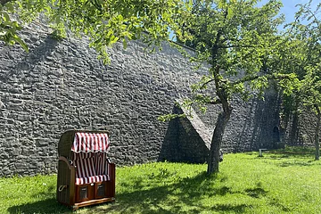 Ein Strandkorb steht auf der grünen Wiese im Stadtgraben. Bäume spenden Schatten.