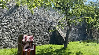 Ein Strandkorb steht auf der grünen Wiese im Stadtgraben. Bäume spenden Schatten.