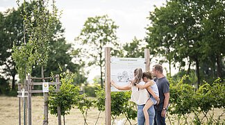 Eine Familie steht an einer Informationstafel im botanischen Obstlehrgarten.