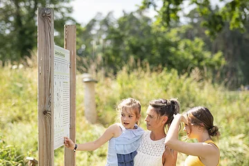 Eine Familie betrachtet eine Informationstafel im botanischen Obstlehrgarten und schafft sich einen Überblick.
