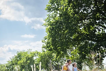 Eine Familie sitzt auf einer Bank in einer Wiese und blickt in die Ferne.