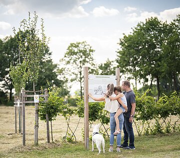Besuch im Obstlehrgarten Eine Familie steht an einer Informationstafel im botanischen Obstlehrgarten.