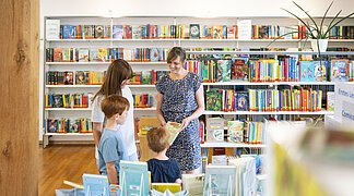 Stadtbüchereileiterin Frau Hertle berät eine Frau mit ihren Kindern zu bestimmten Büchern in der Stadtbücherei.