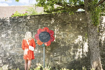 Eine Frau macht einen Spaziergang im Stadtgraben. Hier bleibt sie an einer Blume stehen und liest den Spruch durch.