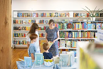 Stadtbüchereileiterin Frau Hertle berät eine Frau mit ihren Kindern zu bestimmten Büchern in der Stadtbücherei.