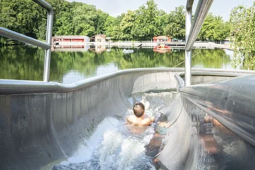 Ein Kind rutscht auf der Wasserrutsche am Waldsee herunter.