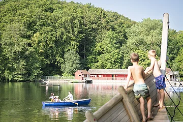 Zwei Kinder stehen auf dem Piratenschiff und beobachten ein Ruderboot, dass auf dem Waldsee in Wemding fährt.