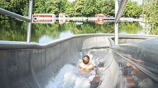 Ein Kind rutscht auf der Wasserrutsche am Waldsee herunter.