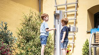 Zwei Kinder bedienen sich am Trinkwasserspender im Innenhof der Tourist-Information.