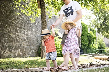 Ein Vater läuft mit seinen zwei Kinder auf dem Barfußpfad im Stadtgraben.