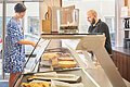 Ein Mann bedient eine Kundin an der Kuchentheke beim Lieblingsgrieche.