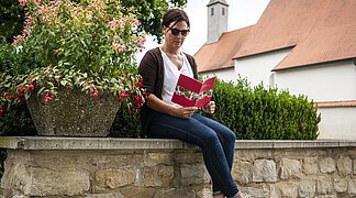 Eine Frau sitzt auf der Mauer neben einer Fuchsienpflanze gegenüber vom Karmelitinnenkloster.