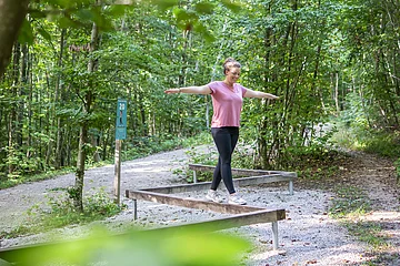 Eine Frau balanciert auf einem Hindernis auf dem Trimm-Dich-Pfad.