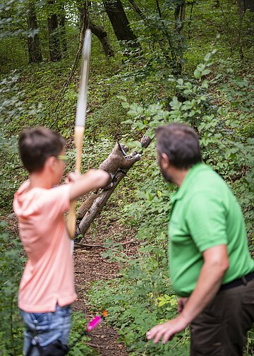 Bogenschieß-Parcour Ein Mann bringt einem Kind das Bogenschießen bei.