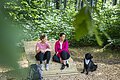 Zwei Freundinnen sitzen mit ihrem Hund auf einer Liege im Wald.