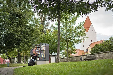 Eine Frau steht mit ihrem Hund am Bücherschrank im Stadtgraben Wemding.