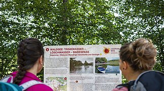 Zwei Freundinnen lesen die Informationstafel "Sagenweg" am Waldsee.