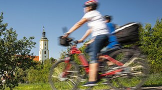 Zwei Radfahrer fahren in die Richtung der Wallfahrtsbasilika Maria Brünnlein bei schönem Wetter.
