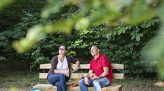 Ein Paar sitzt auf einer Bank im Wald bei schönem Wetter und macht eine kurze Ruhepause.