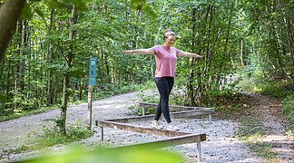 Eine Frau balanciert auf einem Hindernis auf dem Trimm-Dich-Pfad.