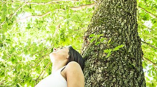 Eine Frau lehnt sich gegen einen Baum und genießt die Ruhe des Waldes.
