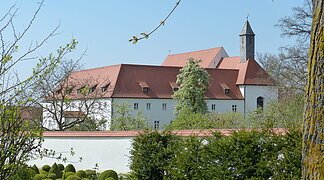 Blick auf den Gebäudekomplex des Klosters in Wemding. Im Vordergrund grüne Büsche und Bäume.