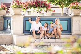 Familie macht ein Selfie am historischen Marktplatz. Im Hintergrund ist der Marienbrunnen zu sehen.