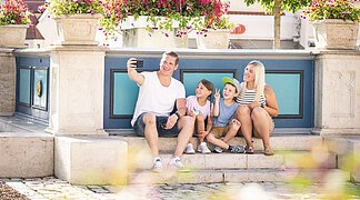 Familie macht ein Selfie am historischen Marktplatz. Im Hintergrund ist der Marienbrunnen zu sehen.