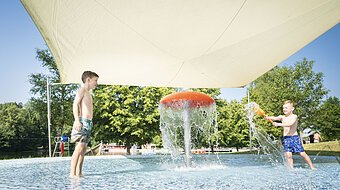 Zwei Kinder spielen mit Wasser am Kinderbecken am Waldsee.