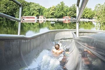 Ein Kind rutscht auf der Wasserrutsche am Waldsee herunter.