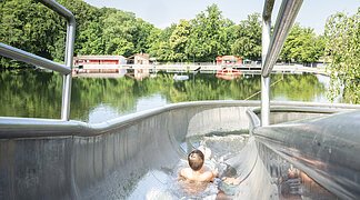 Ein Kind rutscht auf der Wasserrutsche am Waldsee herunter.