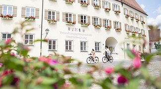 Zwei Radfahrer fahren am Verwaltungsgebäude mit ihrem Fahrrad vorbei.