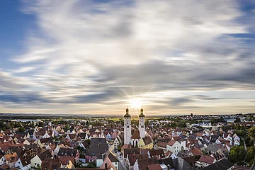 Panoramablick auf Stadt mit roten Dächern und zwei Kirchtürmen bei Sonnenuntergang unter bewölktem Himmel