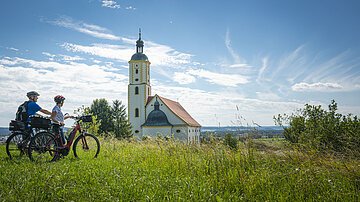 Zwei Radfahrer genießen die Aussicht oberhalb der Wallfahrtsbasilika Maria Brünnlein.