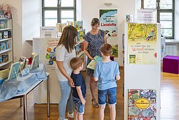 Stadtbüchereileitung Frau Hertle berät eine Frau mit ihren Kindern zu bestimmten Büchern.