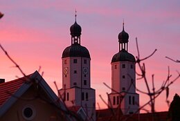 Ein lila-pink leuchtender Sonnenuntergang mit zwei Kirchtürmen.