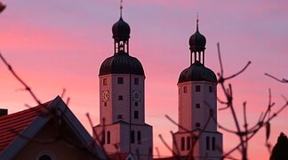 Ein lila-pink leuchtender Sonnenuntergang mit zwei Kirchtürmen.