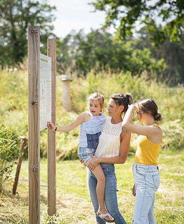 Eine Familie betrachtet eine Informationstafel im botanischen Obstlehrgarten und schafft sich einen Überblick.