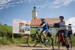 Zwei Radfahrer fahren an der Informationstafel des Sagenwegs vorbei.